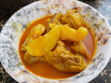 Geleneksel Malezya usulü körili tavuk, beyaz çiçekli bir tabakta servis edilir. Yemek soslu ve büyük doğranmış patatesle kaplı.. 