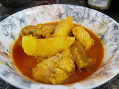 Geleneksel Malezya usulü körili tavuk, beyaz çiçekli bir tabakta servis edilir. Yemek soslu ve büyük doğranmış patatesle kaplı.. 