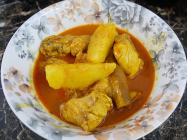 Geleneksel Malezya usulü körili tavuk, beyaz çiçekli bir tabakta servis edilir. Yemek soslu ve büyük doğranmış patatesle kaplı.. 