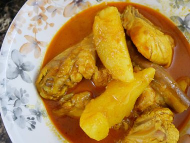 Geleneksel Malezya usulü körili tavuk, beyaz çiçekli bir tabakta servis edilir. Yemek soslu ve büyük doğranmış patatesle kaplı.. 