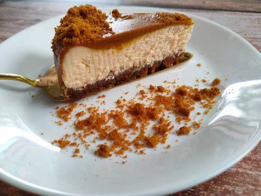 Biscoff Cheesecake 'in seçilmiş dilimleri beyaz bir tabağa konur. Tabağa rastgele esmer şeker serpiştirilmiş..