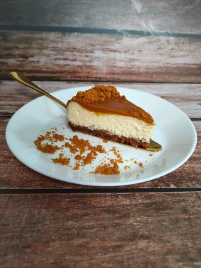 Biscoff Cheesecake 'in seçilmiş dilimleri beyaz bir tabağa konur. Tabağa rastgele esmer şeker serpiştirilmiş..