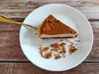 Biscoff Cheesecake 'in seçilmiş dilimleri beyaz bir tabağa konur. Tabağa rastgele esmer şeker serpiştirilmiş..