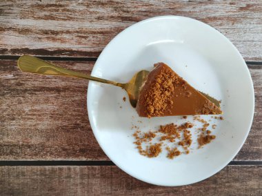 Biscoff Cheesecake 'in seçilmiş dilimleri beyaz bir tabağa konur. Tabağa rastgele esmer şeker serpiştirilmiş..