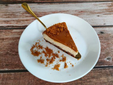 Biscoff Cheesecake 'in seçilmiş dilimleri beyaz bir tabağa konur. Tabağa rastgele esmer şeker serpiştirilmiş..