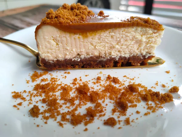 Biscoff Cheesecake 'in seçilmiş dilimleri beyaz bir tabağa konur. Tabağa rastgele esmer şeker serpiştirilmiş..