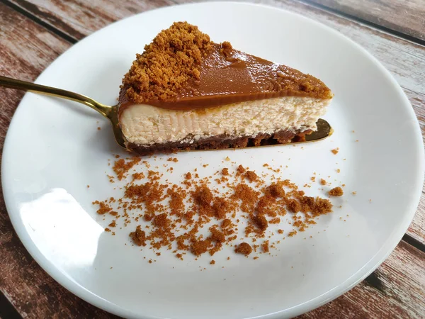 Biscoff Cheesecake 'in seçilmiş dilimleri beyaz bir tabağa konur. Tabağa rastgele esmer şeker serpiştirilmiş..
