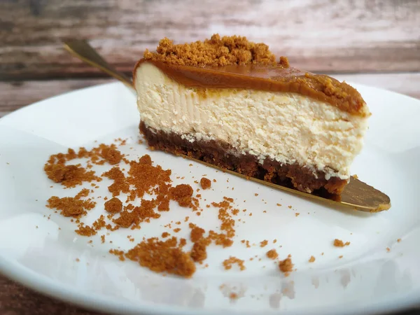 Biscoff Cheesecake 'in seçilmiş dilimleri beyaz bir tabağa konur. Tabağa rastgele esmer şeker serpiştirilmiş..