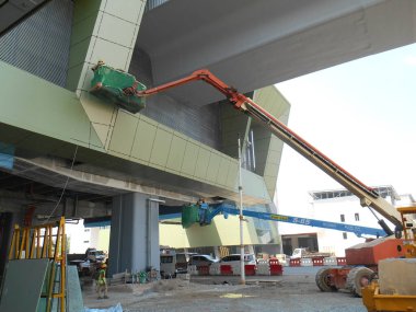 JOHOR, MALAYSIA -16 Mayıs 2017: İnşaat işçileri inşaat alanında yüksek bir seviyede çalışırken taşınabilir vinç kovasında duruyorlar. İşçilerin kendileri tarafından kontrol edilen kova hareketi..  