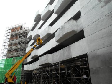 JOHOR, MALAYSIA -16 Mayıs 2017: İnşaat işçileri inşaat alanında yüksek bir seviyede çalışırken taşınabilir vinç kovasında duruyorlar. İşçilerin kendileri tarafından kontrol edilen kova hareketi..  