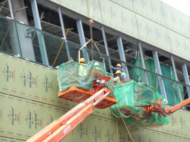 MALACCA, MALAYSIA - 16 Şubat 2017: İnşaat işçileri inşaat alanında yüksek bir seviyede çalışırken taşınabilir vinç kovasında duruyorlar. İşçilerin kendileri tarafından kontrol edilen kova hareketi..  