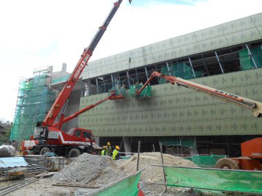 MALACCA, MALAYSIA - 16 Şubat 2017: İnşaat işçileri inşaat alanında yüksek bir seviyede çalışırken taşınabilir vinç kovasında duruyorlar. İşçilerin kendileri tarafından kontrol edilen kova hareketi..  
