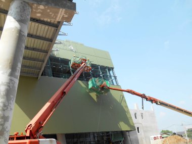 MALACCA, MALAYSIA - 16 Şubat 2017: İnşaat işçileri inşaat alanında yüksek bir seviyede çalışırken taşınabilir vinç kovasında duruyorlar. İşçilerin kendileri tarafından kontrol edilen kova hareketi..  