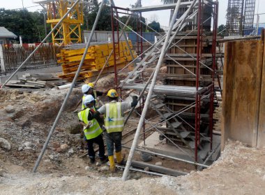 MALACCA, MALAYSIA - 25 Şubat 2017: İnşaat işçileri gün içinde şantiyede çalışıyor. Güvenliklerini sağlamak için düzgün ve uygun güvenlik giysileri giymeleri gerekiyor..  