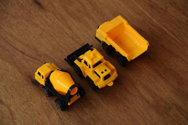 Küçük bir inşaat makinesi oyuncağı, kamyon, buldozer ve beton karıştırıcı grubu. Hepsi de ahşap dokuda izole edilmiş plastikten yapılmış..