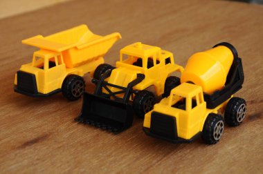 Küçük bir inşaat makinesi oyuncağı, kamyon, buldozer ve beton karıştırıcı grubu. Hepsi de ahşap dokuda izole edilmiş plastikten yapılmış..