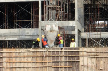 SELANGOR, MALAYSIA - 16 Eylül 2016: İnşaat alanındaki kereste biçimine beton kova kullanarak ıslak beton döken bir grup inşaat işçisi.  