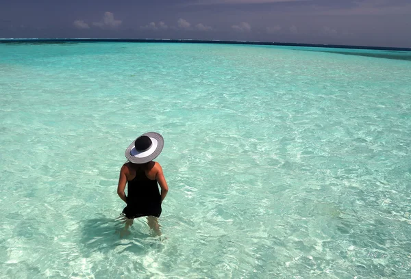Женщина в шляпе, стоящая в океане и смотрящая на горизонт — стоковое фото