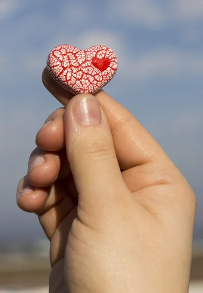 Mano sosteniendo un corazón moteado rojo contra el cielo azul — Foto de Stock