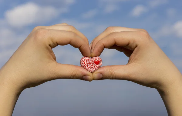 Two hands holding a red speckled heart against the blue sky — Stock Photo, Image