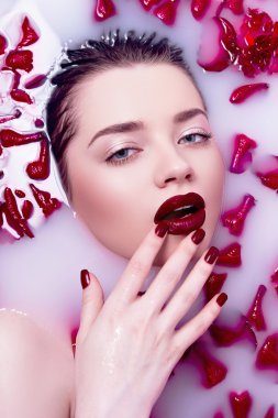Gül yaprakları ile bir banyoda kız. Su süt ile. Kırmızı ruj ve kırmızı tırnak.