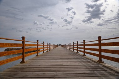 Bulutlu bulutlu bir gökyüzünün arka planına karşı masmavi denizin üzerindeki ahşap iskele..