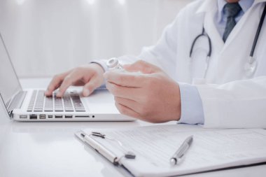 Doctor doing paperwork and using laptop in clinic. description into a server computer in hospital. Concept invented a cure, vaccine for coronavirus disease (COVID-19).