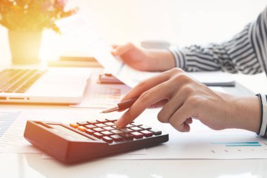 Business woman using calculator and writing make note with calculate. taxes and economic concepts. Savings, finances and economy concept through a laptop.