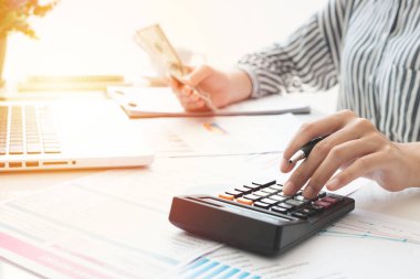 Business woman using calculator and writing make note with calculate. taxes and economic concepts. Savings, finances and economy concept through a laptop.