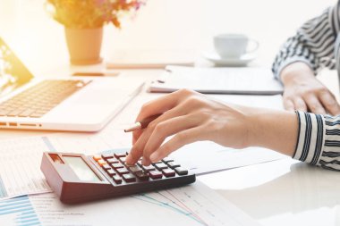 Business woman using calculator and writing make note with calculate. taxes and economic concepts. Savings, finances and economy concept through a laptop.