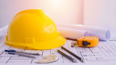 Sarı başlık ve çalışma masasına bir sürü çizim. Proje belgeleri ve aletler yanında. Ortada boş yer var. İnşaat arka planında düz yatıyordu. Mühendislik aletleri. Boşluğu kopyala