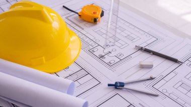 Sarı başlık ve çalışma masasına bir sürü çizim. Proje belgeleri ve aletler yanında. Ortada boş yer var. İnşaat arka planında düz yatıyordu. Mühendislik aletleri. Boşluğu kopyala