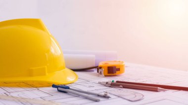 Sarı başlık ve çalışma masasına bir sürü çizim. Proje belgeleri ve aletler yanında. Ortada boş yer var. İnşaat arka planında düz yatıyordu. Mühendislik aletleri. Boşluğu kopyala