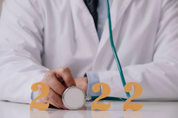 Doktor masasında 2022 numaralı steteskop tutan beyaz üniformalı doktor. Sağlık ve tıbbi konsept için mutlu yıllar..