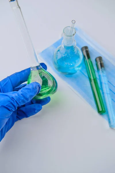 Επιστήμονας που κρατάει φιάλη και σωλήνα στο εργαστήριο, κοντινό πλάνο. Χημεία λύσης. Αντιιικό διάλυμα. Γαλάζιο και πράσινο υγρό — Φωτογραφία Αρχείου