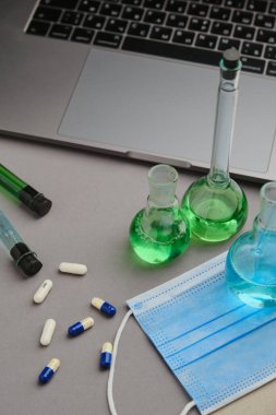 Yeşil, mavi sıvı ve haplarla dolu bir laboratuvar şişesi. Virüs tedavisi ve dizüstü bilgisayar araştırması