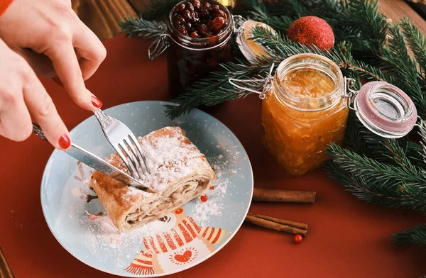 Closeup corte comer strudel em um prato de Natal perto de jarros de engarrafamento. Café da manhã. Mesa vermelha — Fotografia de Stock