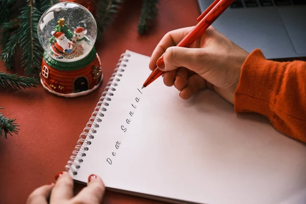 Woman at home office is writing a letter to Santa on Christmas. Snow globe and laptop nearby — Stock Photo, Image