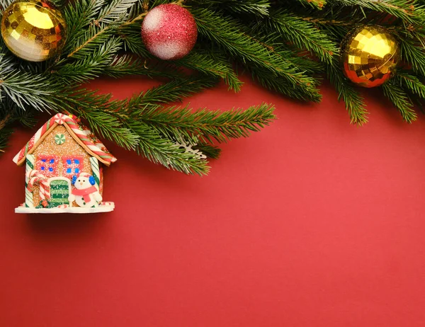 Flat lay with pine tree branches with red and golden Christmas balls isolated on red and a toy house — Stock Photo, Image