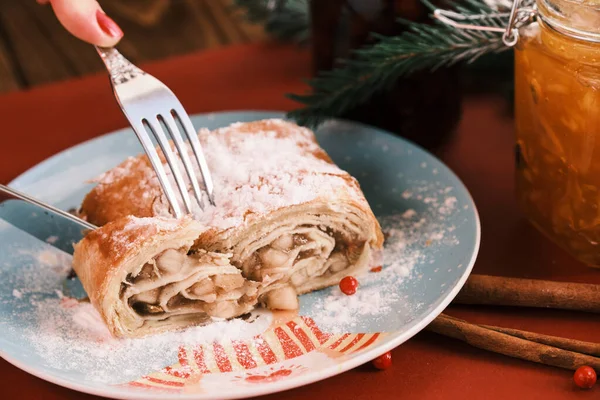 Closeup corte comer strudel em um prato de Natal perto de jarros de engarrafamento. Café da manhã. Mesa vermelha — Fotografia de Stock