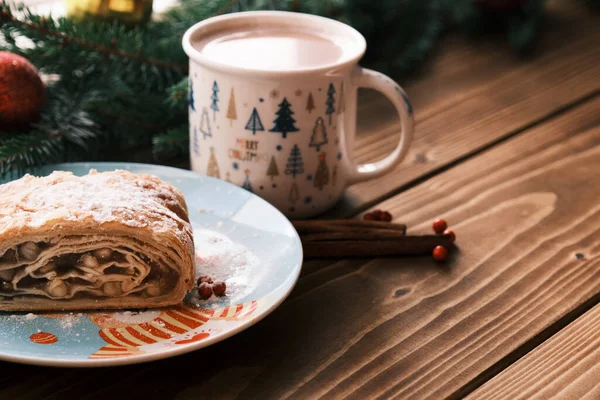 Feche de um strudel em uma chapa de Natal perto de paus de canela e chocolate quente. Café da manhã Natal — Fotografia de Stock