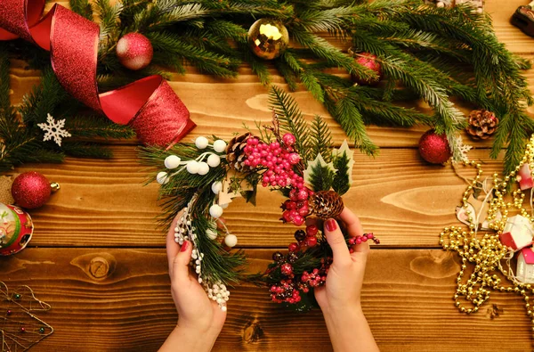 Hands making rustic Christmas wreath s on a wooden background. Atmospheric moody image at holiday workshop — Stock Photo, Image