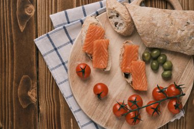 Kaba ahşap arka planda füme somonlu iki sandviç ve diğer yiyecekler. Üst görünüm
