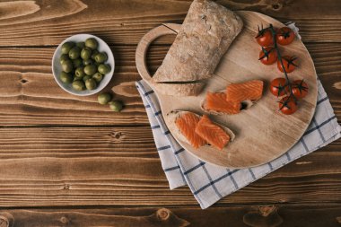 Kaba ahşap arka planda füme somonlu iki sandviç ve diğer yiyecekler. Üst görünüm