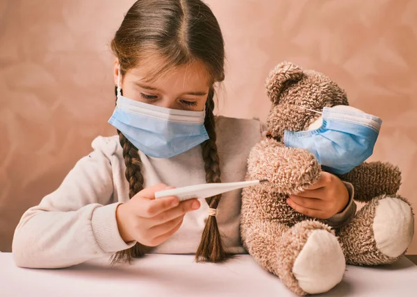 Läkare flicka i mask leka och mäta temperaturen på en leksak björn Stockbild