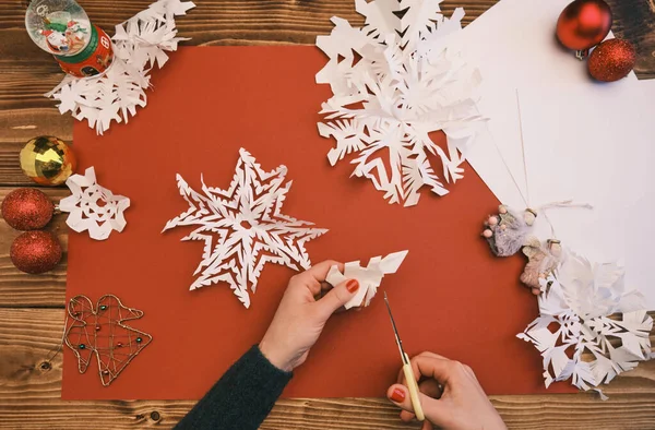 Female Hands making white paper snowflakes over wooden table — Stock Photo, Image