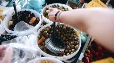 Bir kadının markette zeytin toplayıp plastik bir torbaya koyması..