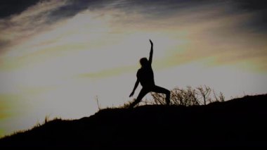 Gün doğumunda kum tepelerinde yoga yapan bir kadının silueti. İHA atışı. Havadan. 