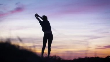 Gün doğumunda kum tepelerinde yoga yapan bir kadının silueti. 4K çözünürlüğünde çekilen.