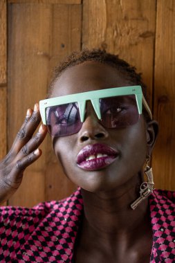 Pembe ceketli güzel siyah manken ve objektife bakarken abartılı güneş gözlüğü takıyor. Tabanca küpesi. Yüksek kalite fotoğraf